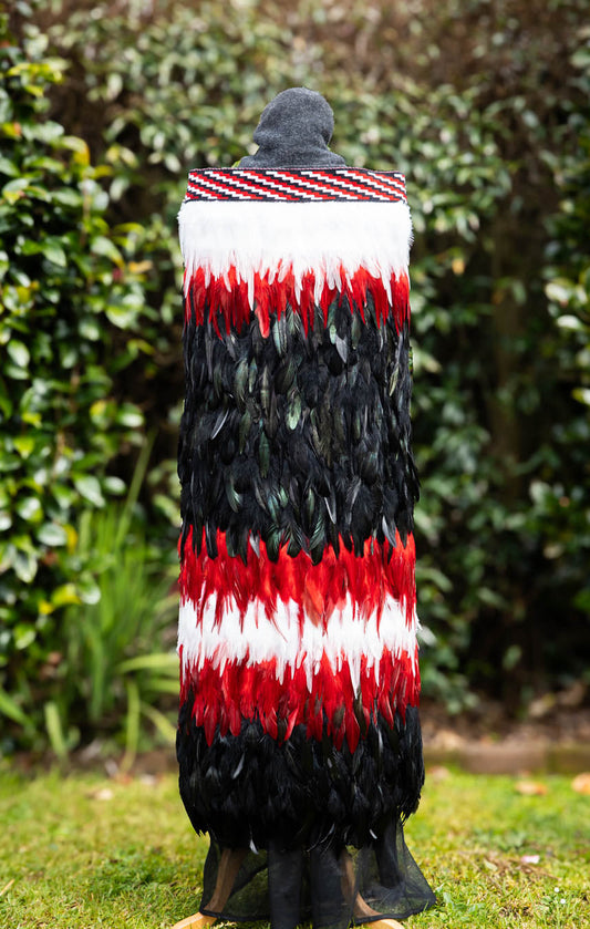 Person wearing a colorful feathered cape in a garden setting