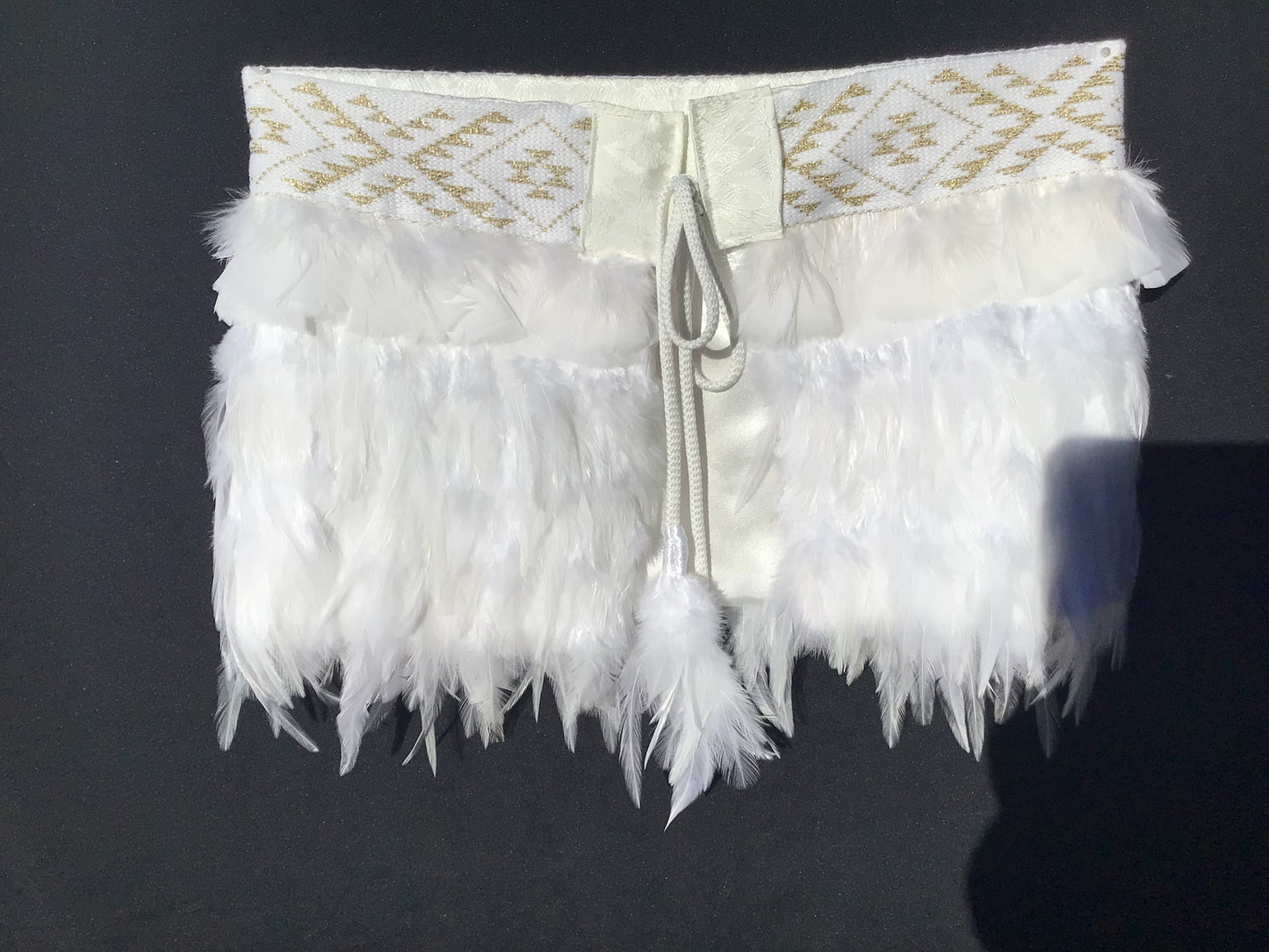 White feathered item with gold embroidery on a dark background