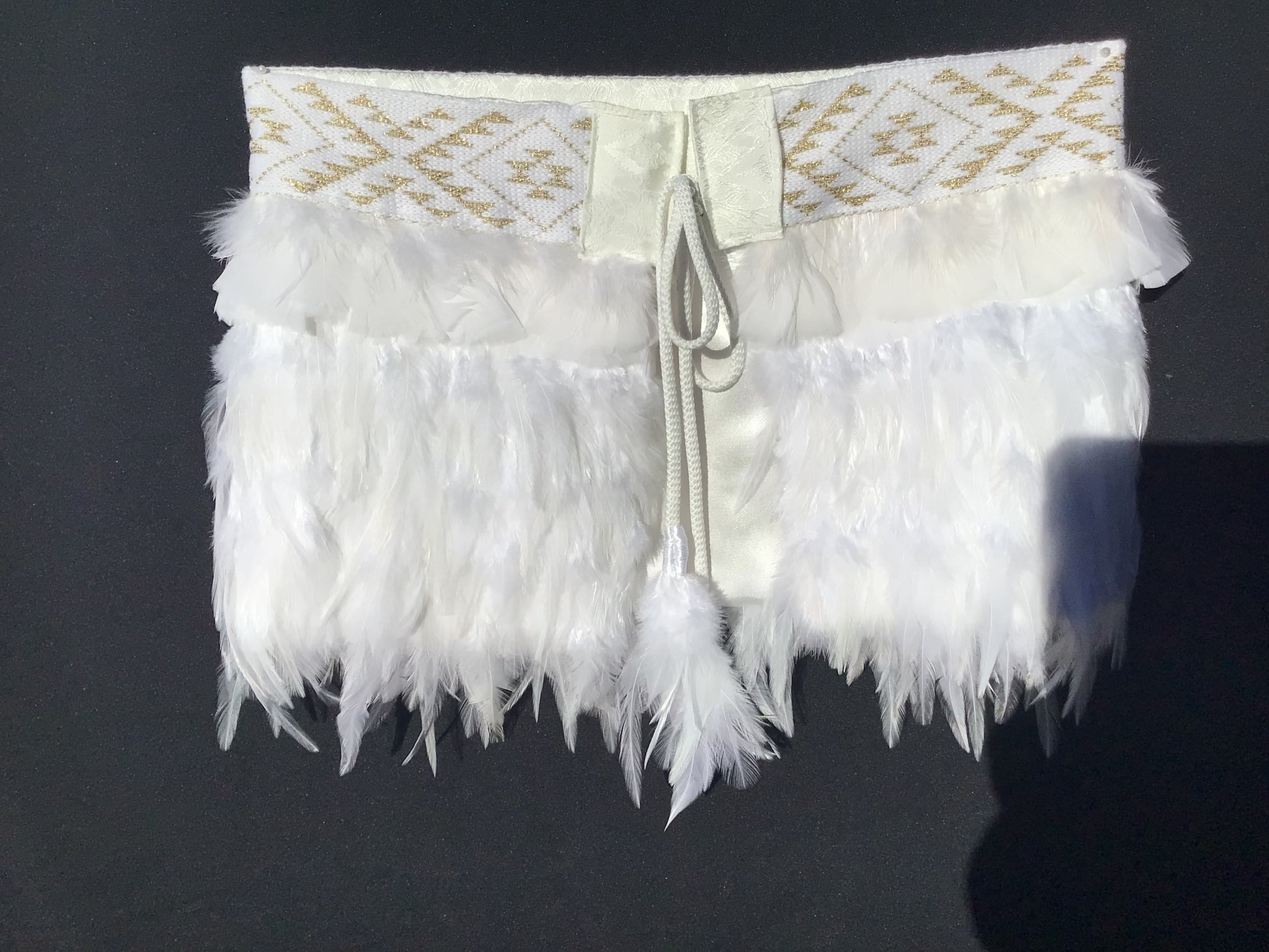 White feathered item with gold embroidery on a dark background